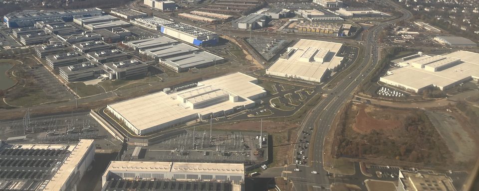 Aerial view of a data-center campus beside a substation, with cleared land alongside